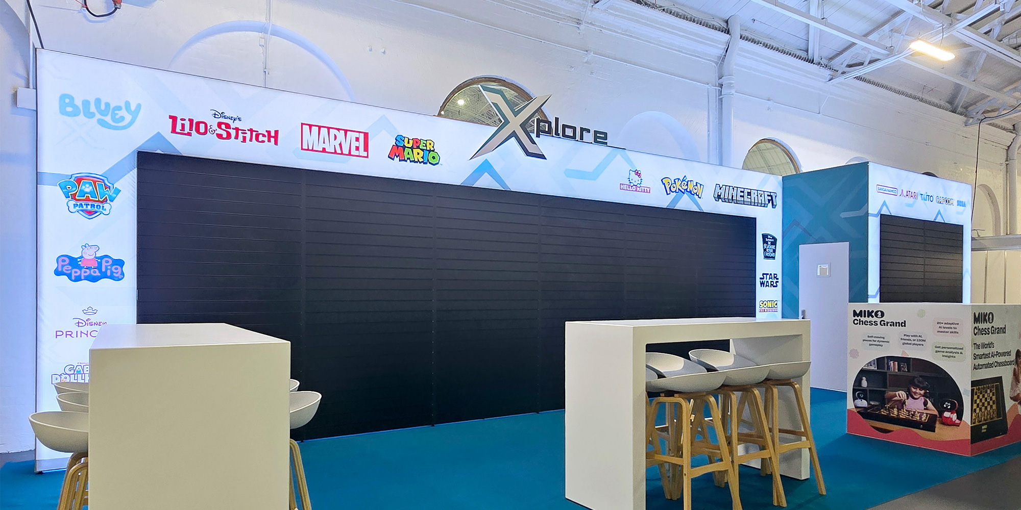 Modular exhibition stand with integrated black slatwall panels and illuminated branded lightbox fascia for Xplore Brands at Toy Fair.